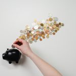 黒い豚の貯金箱に、床に広がった小銭の一つを入れようとしている写真
