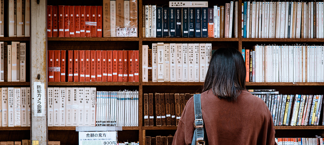 古本屋の本棚の前に人物が立つ風景