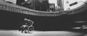 コンクリートの坂道を車椅子で進む男性のモノクロ写真